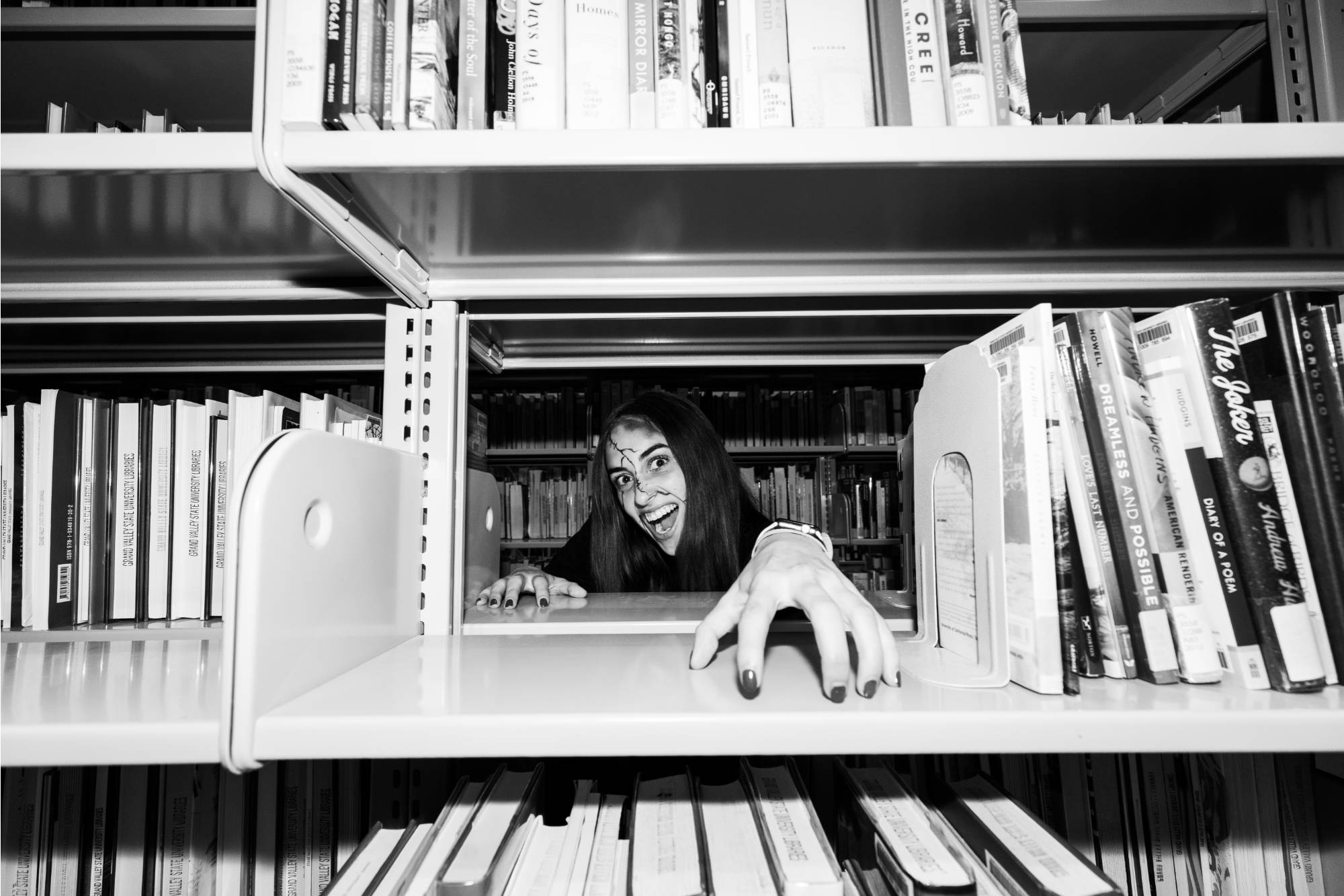 girl in zombie make-up reaching through books on bookshelf